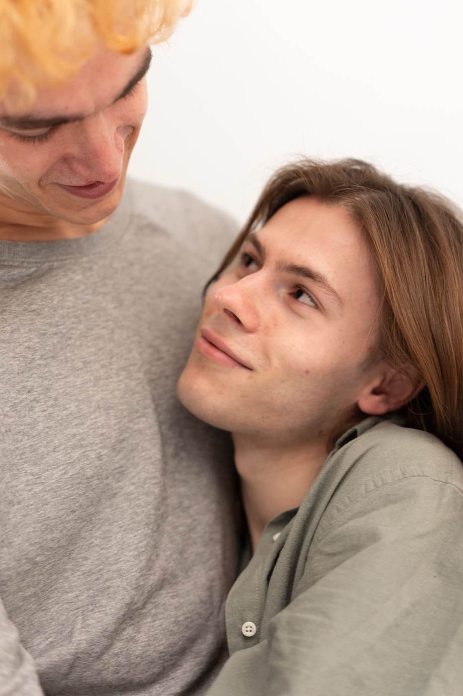 Two young men in a tender embrace, one leaning his head against the other's chest
